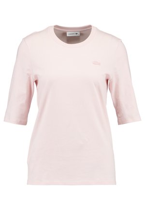 T-shirt à manches courtes rose clair en coton doux, avec un col rond et le logo Lacoste brodé sur la poitrine.
