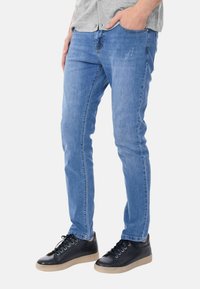 Jeans in denim blu con un fit slim, caratterizzati da una chiusura con bottone e una leggera abrasione. Abbinati a sneakers nere con lacci.