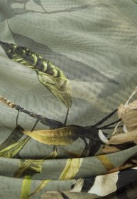 Durchsichtiges Material mit einem botanischen Muster aus grünen Blättern und erdigen Tönen, das eine zarte Textur und subtile Transparenz zeigt.