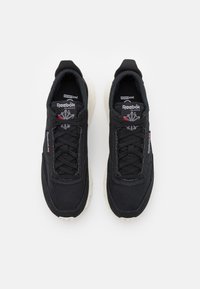 Zapatillas deportivas negras con un upper texturizado, diseño de cordones y suelas de goma color crema. Logotipo de Reebok en la lengüeta.