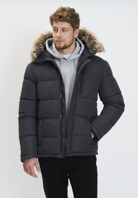 Chaqueta de plumas negra con capucha forrada de piel, que cuenta con un cierre de cremallera y botones a presión, textura acolchada y bolsillos laterales. Sudadera gris debajo.
