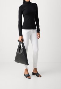 Svart långärmad polotröja med figurnära passform, tillsammans med vita slim fit jeans, håller en stor svart läderhandväska och bär svarta klackar.