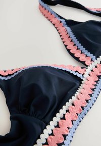 Mornarica bikini vrh s valovitim rubom u ružičastoj, svijetloplavoj i bijeloj boji. Glatka tekstura s naboranim detaljima u središtu.