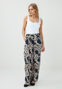Witte mouwloze top gecombineerd met marineblauwe, patroonrijke wijde broek met abstracte ontwerpen in crème en bruin, met zijzakken en elastische tailleband.