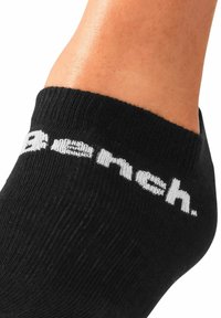 Schwarze Knöchelstrümpfe mit geripptem Material und weißem Markenlogo am Bündchen. Die Nahaufnahme hebt die Material- und Designmerkmale hervor.