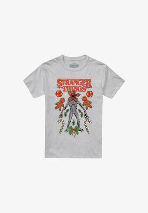Graues T-Shirt mit rotem "Stranger Things"-Text, das einen Demogorgon zeigt, rote Würfel, Lebkuchenmänner, Stechpalmenblätter, Zuckerstangen und eine grüne Schleife enthält.