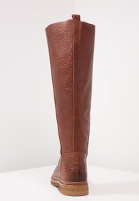 Bruna läderknä-höga stövlar med strukturerad yta, kontrasterande sömmar och en platt sula. Har en sidoseam och förstärkt bakdel.