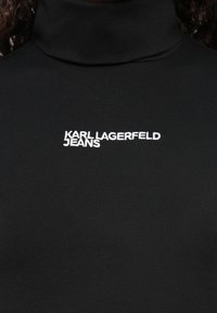 Crni turtleneck majica napravljena od glatkog, rastezljivog materijala, sa bijelim izvezenim natpisom "KARL LAGERFELD JEANS" na prsima.
