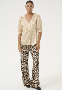 Blusa color oro pallido, struttura testurizzata con maniche a sbuffo e chiusura a bottoni, abbinata a pantaloni a zampa d'elefante con stampa leopardata in tonalità beige e nera.