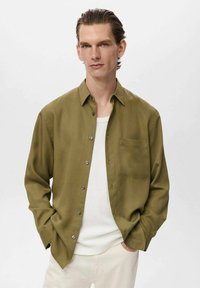 Olive green button-up shirt in smooth fabric, featuring a chest pocket and silver buttons, paired with a white crew neck t-shirt underneath.