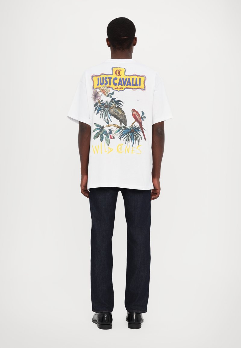 Hvit kortermet t-skjorte med fargerik grafisk utskrift av tropiske fugler og bladverk, med "JUST CAVALLI" merkevare og "WILD ONES" tekst.