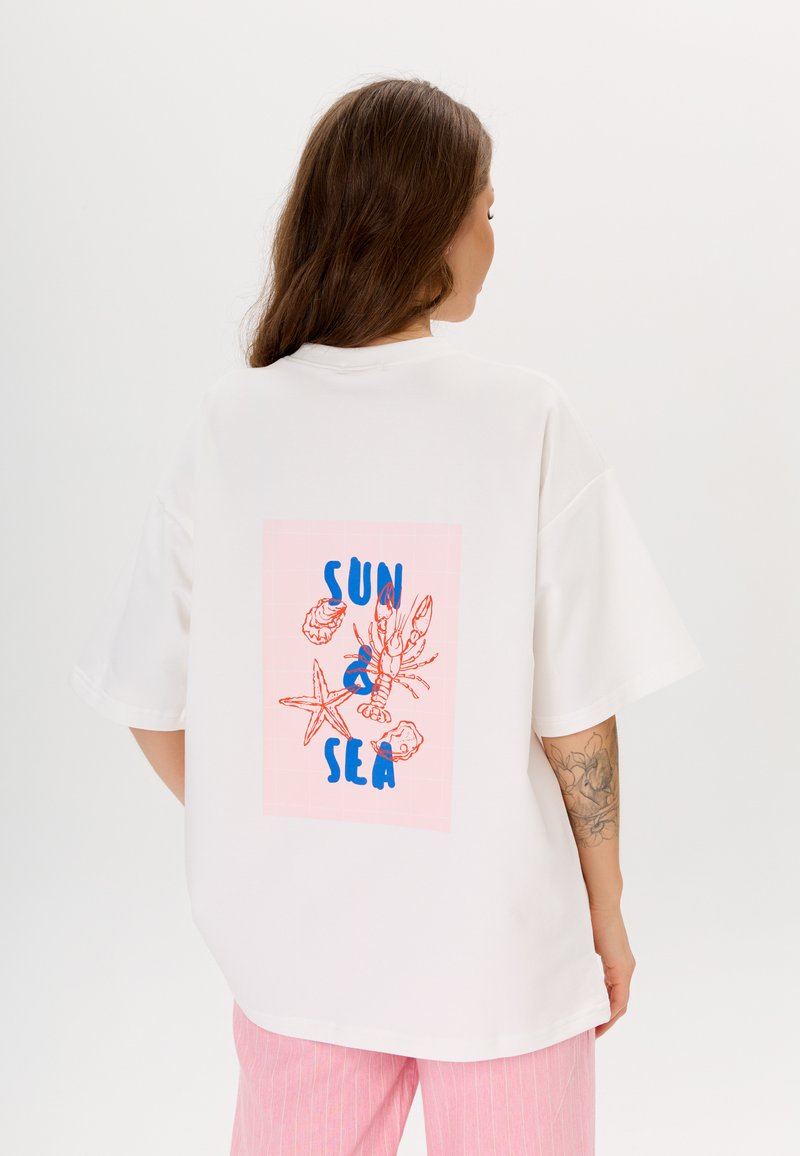 Witte katoenen T-shirt met een roze grafisch ontwerp en blauwe tekst "ZON & ZEE," geïllustreerde zeedieren en relaxte mouwen.