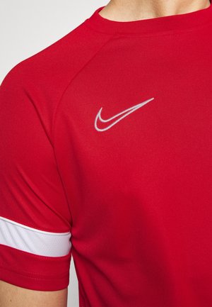 T-shirt de sport rouge avec le logo Nike swoosh blanc sur la poitrine et une bande horizontale blanche sur la manche.
