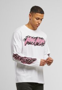 White long-sleeve t-shirt with pink and black graphic logos on the front and sleeves. Made of cotton, featuring a relaxed fit and round neckline.