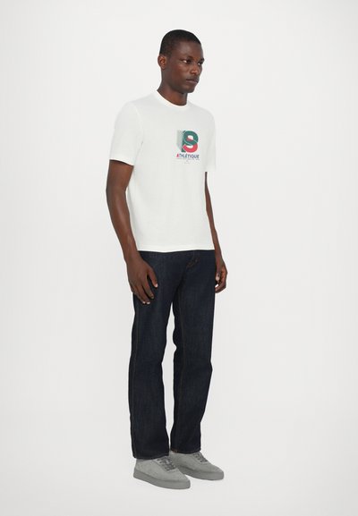 Hvit bomulls t-skjorte med grafisk trykk i rødt, grønt og blått. Sammen med mørkeblå jeans og lysegrå sneakers.