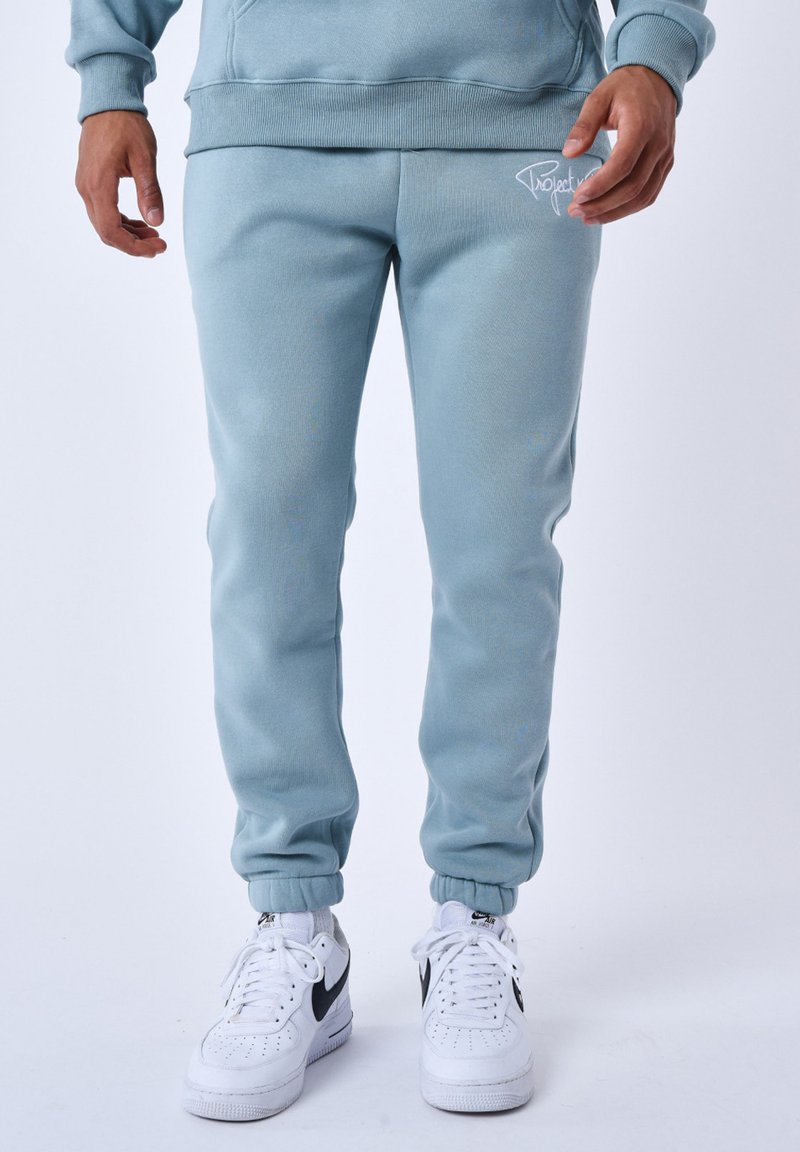 Jogging in cotone azzurro chiaro con polsini a coste, una vita elasticizzata e un logo bianco sulla coscia, abbinati a sneakers bianche.