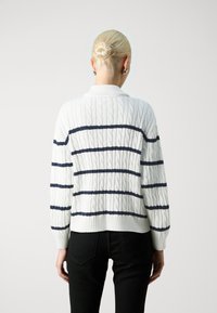 Suéter blanco de punto trenzado con rayas horizontales en azul marino, con cuello y puños de canalé, mostrado desde la parte posterior sobre un fondo liso.