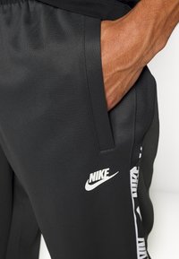 Svarta träningsbyxor i slätt, stretchigt material. Har en sidficka och en vit Nike-logotyp. Kontrasterande mönster på sidodelen.