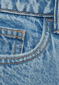 Svetlo modri jeans material vsebuje sprednji žep z oranžnim šivanjem in ukrivljenim šivom, ki prikazuje teksturiran končni izgled in sproščen dizajn.