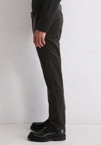 Pantalon en velours côtelé gris foncé avec poches latérales, présentant une coupe droite et des chaussures noires à lacets. La texture est côtelée et douce.