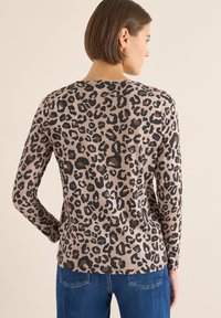 Bluzka z długim rękawem w panterkę w kolorach beżowym i czarnym, o miękkiej fakturze i klasycznym okrągłym dekolcie, zestawiona z dżinsami.