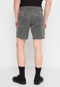 Shorts en denim gris avec une texture délavée, de longueur mi-cuisse, et deux poches arrière. Portés avec des baskets noires et des chaussettes.