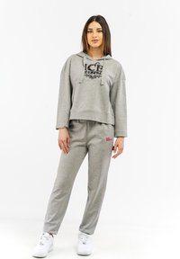 Felpa corta grigia con logo nero e pantaloni della tuta grigi coordinati. Sneakers bianche. Tessuto morbido, vestibilità rilassata, con dettagli di design minimalisti.