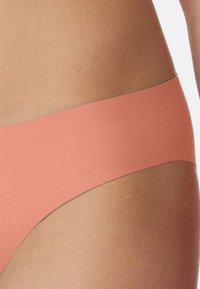Pfirsichfarbene Bikiniunterhose mit glatter Textur und breitem Bund, die ein minimalistisches und nahtloses Design aufweist.