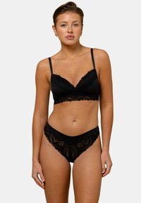 Bralette en dentelle noire avec bretelles ajustables et bords festonnés, associée à un shorty en dentelle assorti. Tissu doux, détails de motifs complexes.