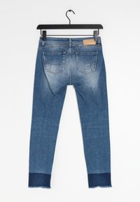 Uzké džíny z modrého denimu s vybledlým vzhledem, se zadními kapsami, třepicí na spodním lemu a kontrastním tmavě modrým akcentem na spodní části.