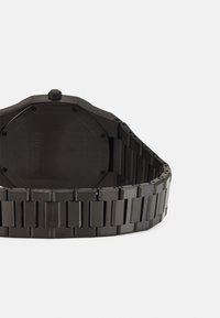 Montre noire octogonale avec finition mate, dotée d'un design de bracelet segmenté. L'arrière est lisse avec des détails de vis.
