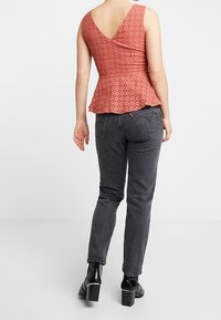 Haut peplum corail avec texture à œillets, dos en V. Associé à un jean gris foncé et des bottines à talons carrés noires.