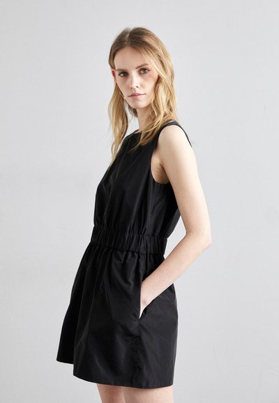 Robe noire sans manches avec une taille élastique, poches latérales et une coupe décontractée. Texture lisse et design à longueur de genoux.