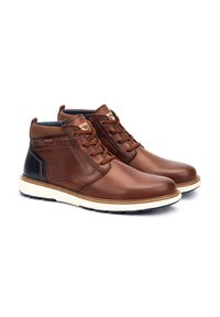 Botas de tobillo de cuero marrón con puntera redondeada, cuello acolchado y acentos de tacón negro contrastantes. Presenta una suela de goma blanca y un diseño de cordones.
