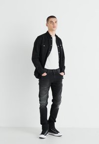 Black button-up shirt over a white t-shirt, paired with faded black jeans and black sneakers. Minimalist design against a white background.