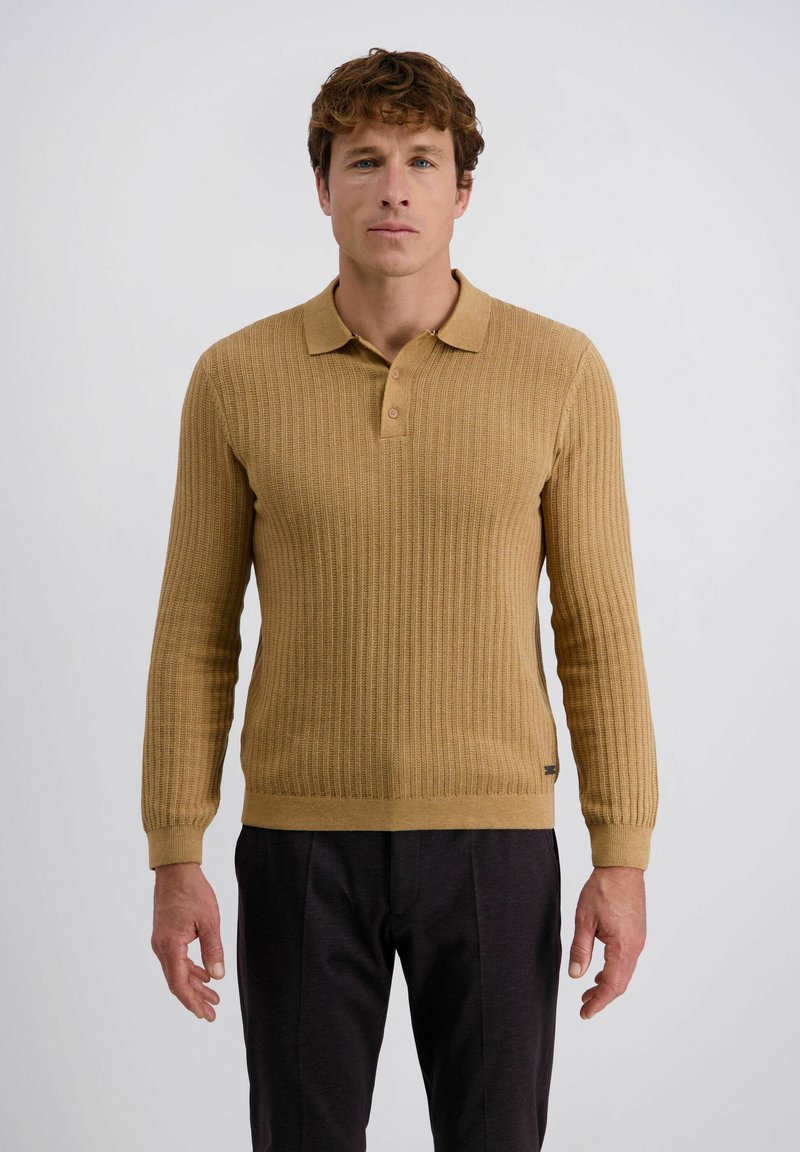 Langärmliger Polo-Sweater aus geripptem senfgelben Strick, mit Kragen und einer Knopfleiste mit drei Knöpfen. Kombiniert mit dunklen Hosen.