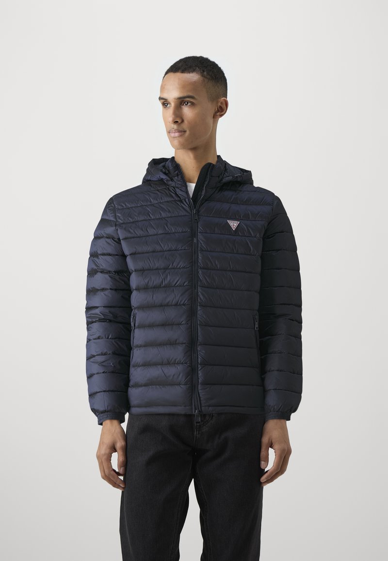 Navy blue puffer jacket with a zip front, elastic cuffs, and a hood. Features a small logo on the chest and quilted pattern throughout.
