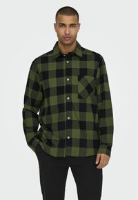 Groen en zwart geruite shirt van een zachte stof, met een knoopsluiting aan de voorkant, kraag en een enkele borstzak. Lange mouwen.