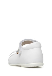 Bílé dětské boty s kulatou špičkou, z koženého materiálu, s suchým zipem a texturovanou podrážkou. Jednoduchý design s minimálními akcenty.