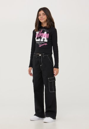 Felpa nera corta con grafica rosa con il testo "CALIFORNIA LA" abbinata a pantaloni cargo neri larghi con tasche laterali e cuciture bianche.