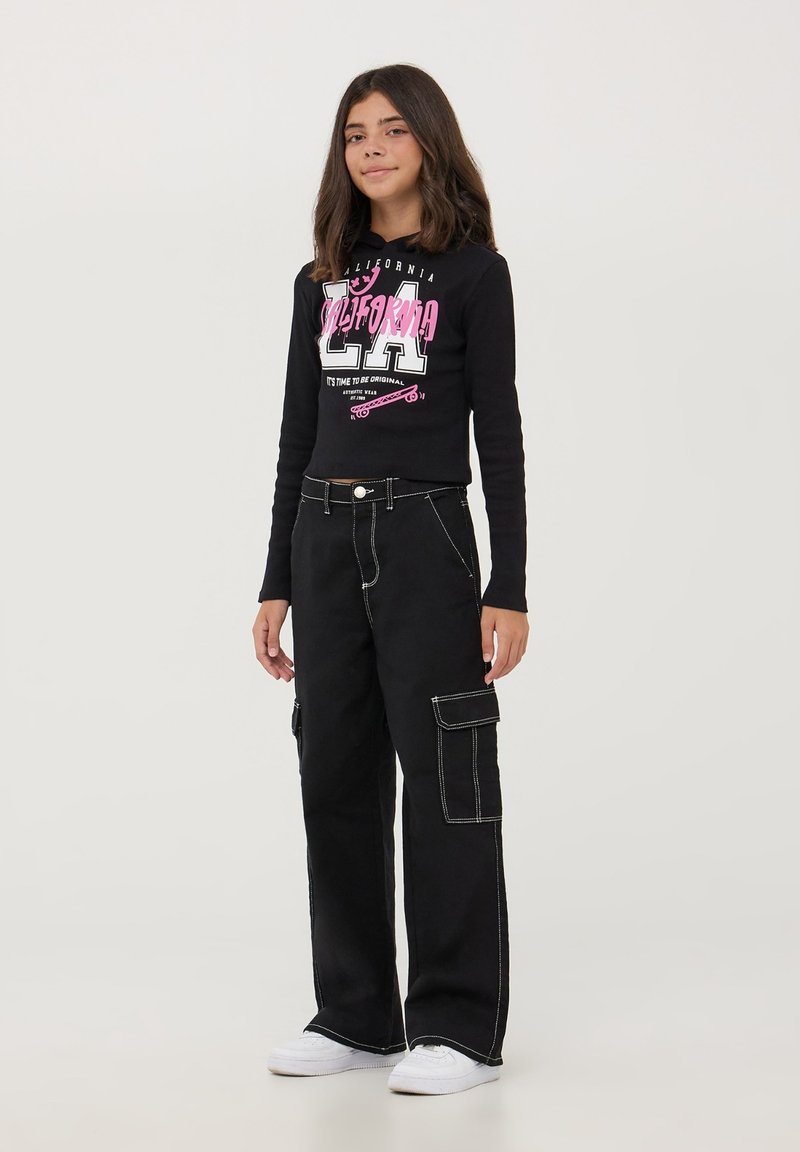 Felpa nera corta con grafica rosa con il testo "CALIFORNIA LA" abbinata a pantaloni cargo neri larghi con tasche laterali e cuciture bianche.