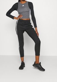 Grå randig crop-top med svarta långa ärmar, parat med svarta avsmalnande träningbyxor med vita sidosträck och svarta sportskor.