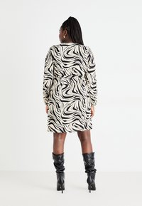 Robe à manches longues en crème avec un motif zèbre noir ondulé, taille cintrée et coupe décontractée, associée à des bottes noires à talons montant jusqu'aux genoux.