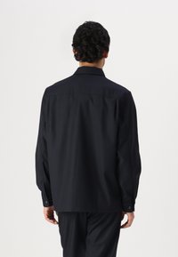 Black long-sleeve shirt with a straight cut, buttoned cuffs, and a classic collar. Made of smooth fabric with minimal texture.