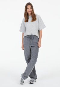 Gray ribbed short-sleeve sweater paired with dark gray drawstring trousers. Model wears light gray athletic shoes. Simple, casual outfit.