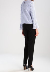 Blusa a righe blu e bianca con maniche a campana, caratterizzata da rifiniture in pizzo e dettagli con bottoni, abbinata a pantaloni neri aderenti e tacchi alti.