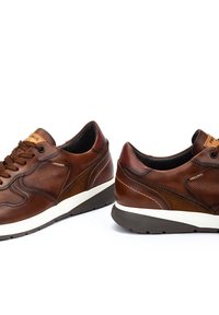 Zapatillas de cuero marrón con un panel texturizado y suela contrastante. Punta redondeada, diseño con cordones y marca Pikolinos en la lengüeta.