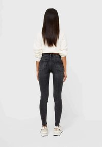 Jeans negros de cintura alta con un ajuste slim, con bolsillos traseros, combinados con un suéter blanco y zapatillas blancas voluminosas.