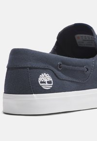 Navy Canvas Sneaker mit weißem gesticktem Logo, Gummisohle und Ösenakzenten für verbesserte Atmungsaktivität und Haltbarkeit.
