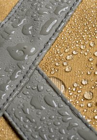 Waterbestendig grijs materiaal met een gestructureerd oppervlak, gelegd bovenop een beige stof, beide met verspreide waterdruppels.